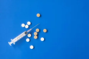 Top view flat lay composition of set of medical syringe and various pills placed on blue background