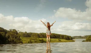 A woman stands with arms raised, enjoying a serene lakeside view in Dalat, Vietnam.