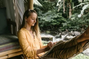Woman in hammock sketching in a peaceful outdoor setting by a river.