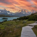 Wooden boardwalk leading to Torres del Paine mountains under a vibrant sunset sky in Chile.