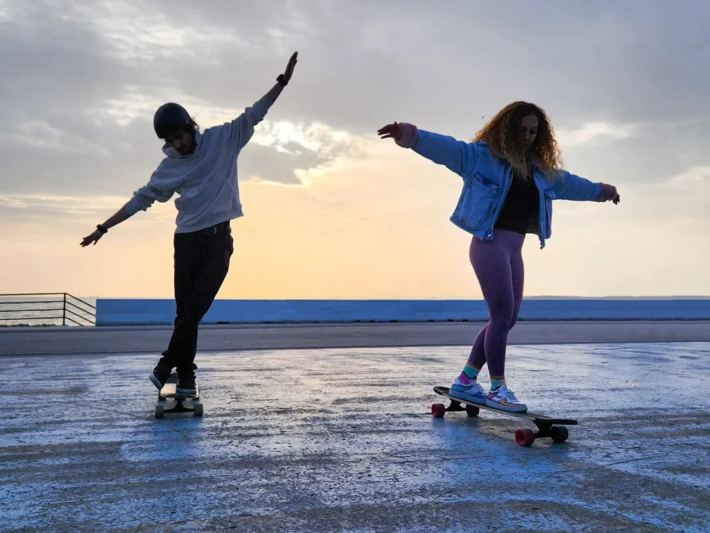 Two young adults skateboarding gracefully on a seaside promenade at sunset in İstanbul, Türkiye.