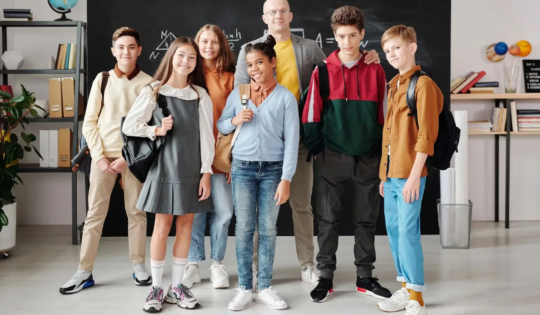 Group of diverse teenagers posing with their teacher in a modern classroom.