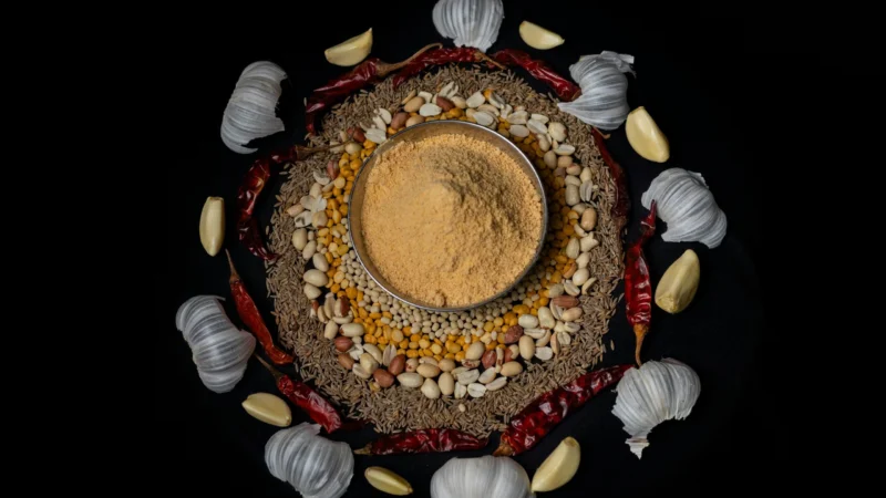 Top view of traditional Indian spices and masala surrounded by garlic and chilies on a dark background.