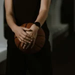 A close-up shot of a basketball player holding a ball in a dimly lit indoor space.