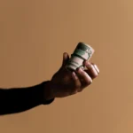 A close-up image showing a hand holding a roll of money against a beige background, ideal for finance themes.