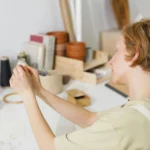 Caucasian woman crafting in a minimalist workspace with sewing supplies and plants.
