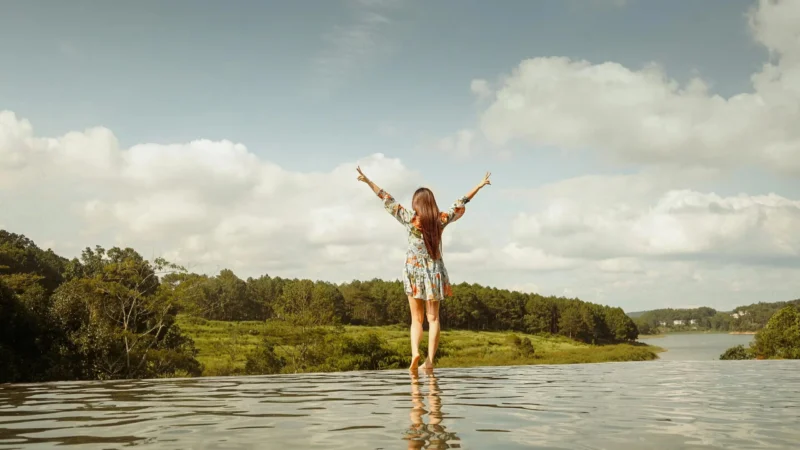 A woman stands with arms raised, enjoying a serene lakeside view in Dalat, Vietnam.