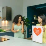 Two women discussing nutrition in a kitchen, holding health-related posters.