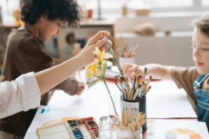 Children painting and drawing together in an art workshop, holding paintbrush and using colors.