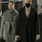 A group of fashionable women in coats standing confidently in an urban environment.