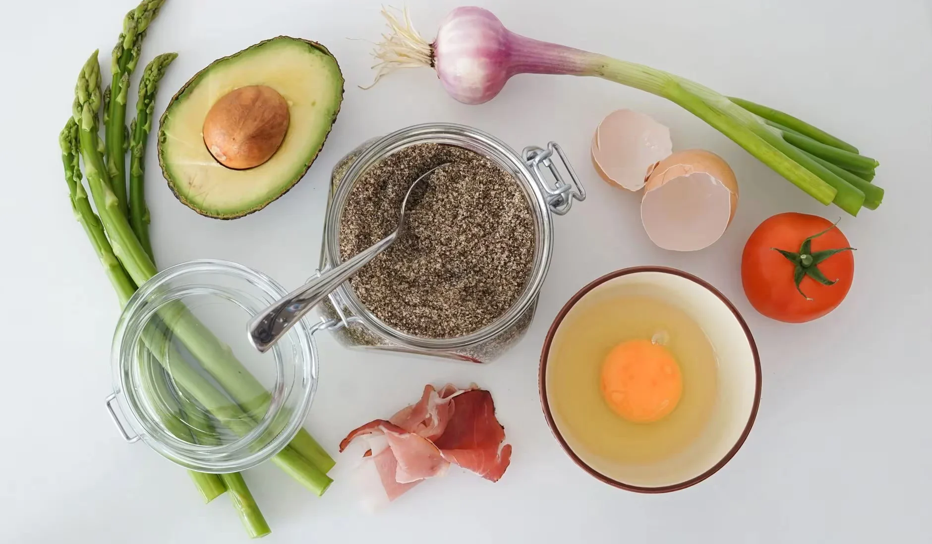Flat lay of fresh asparagus, avocado, egg, tomato, and more for a keto-friendly dish.