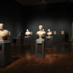 An art gallery with classical sculptures and framed art, showcasing elegant indoor lighting and design.