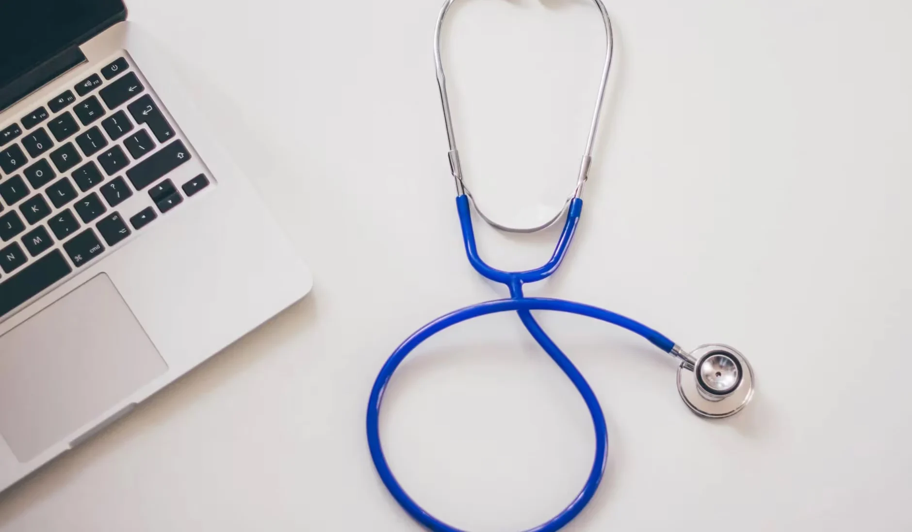 Medical stethoscope and laptop on a white desk, symbolizing digital health solutions.